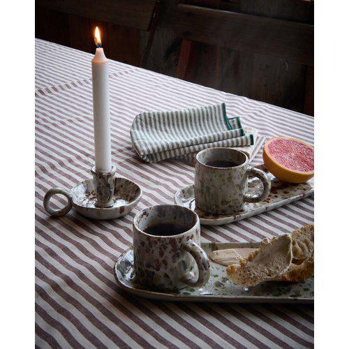 Aila porcelain mugs, a lit candle, and a half-eaten grapefruit on a striped tablecloth.