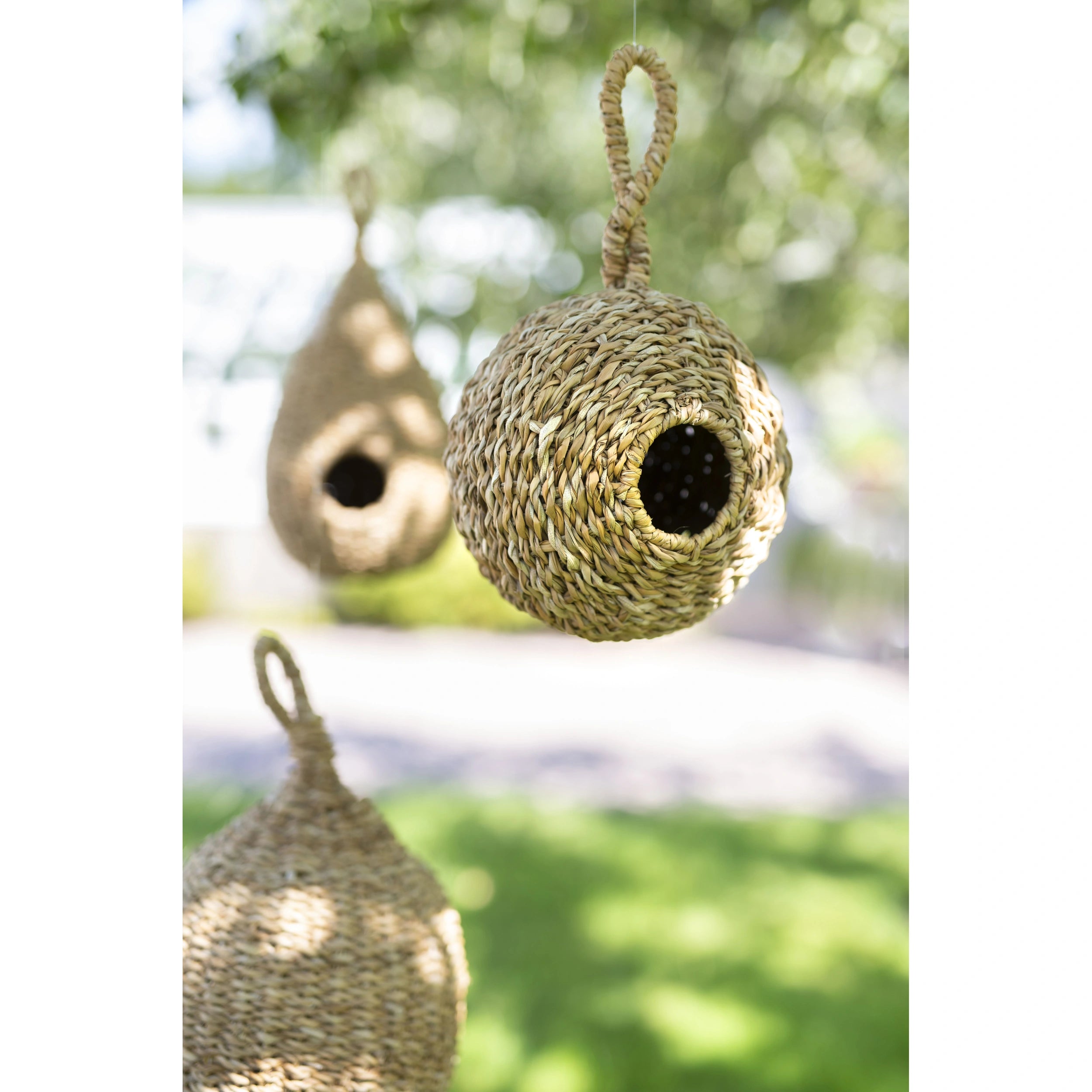 Three woven birdhouses hanging outdoors with a blurred natural background