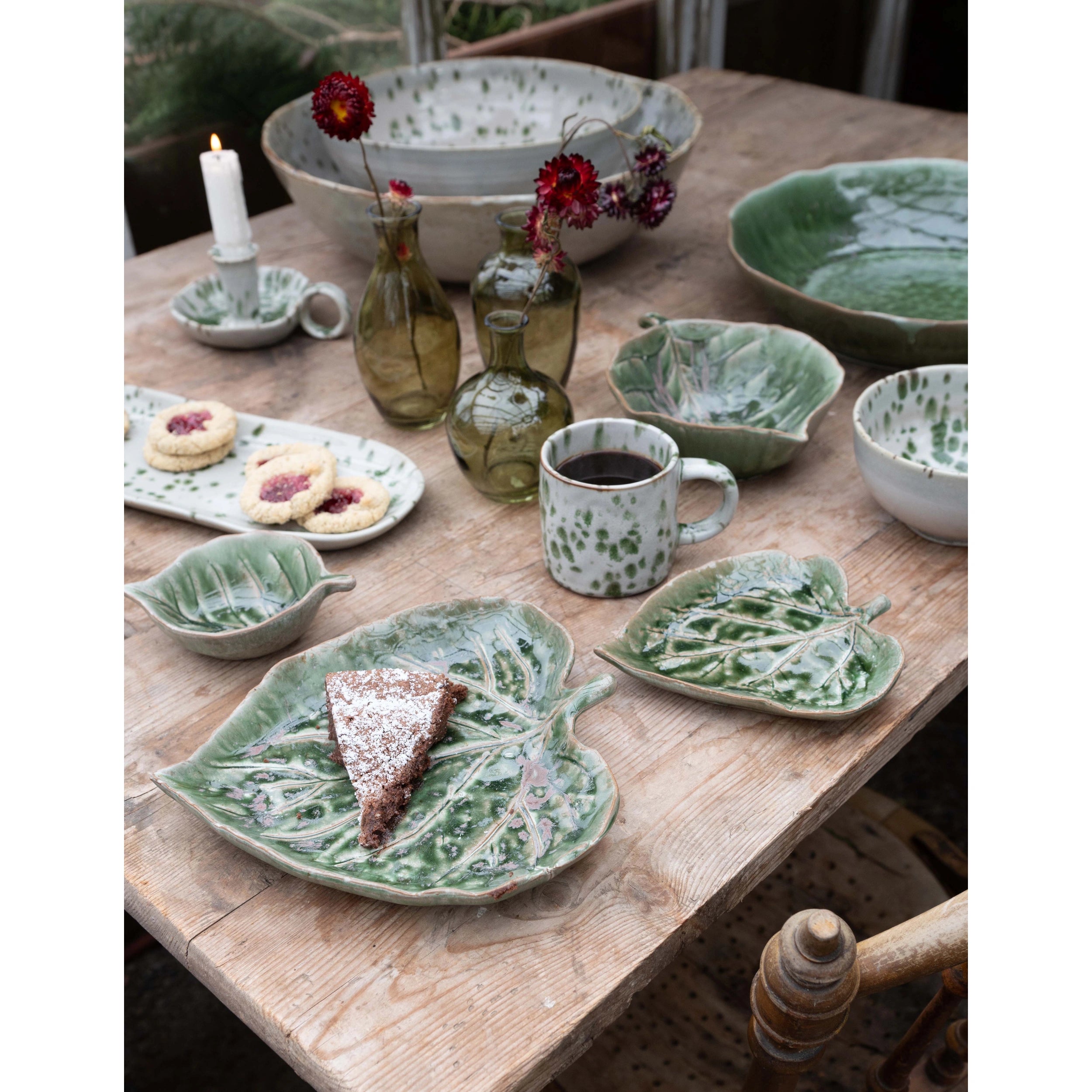 Ceramic tableware including bowls, plates, and aila green speckledmugs on a wooden table with a rustic setting