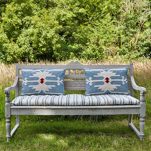Two mid blue kilim inspired rectangular sofa cushions on bohemian wooden sofa outdoors. Shows cushions are suitable for indoor and outdoor use.