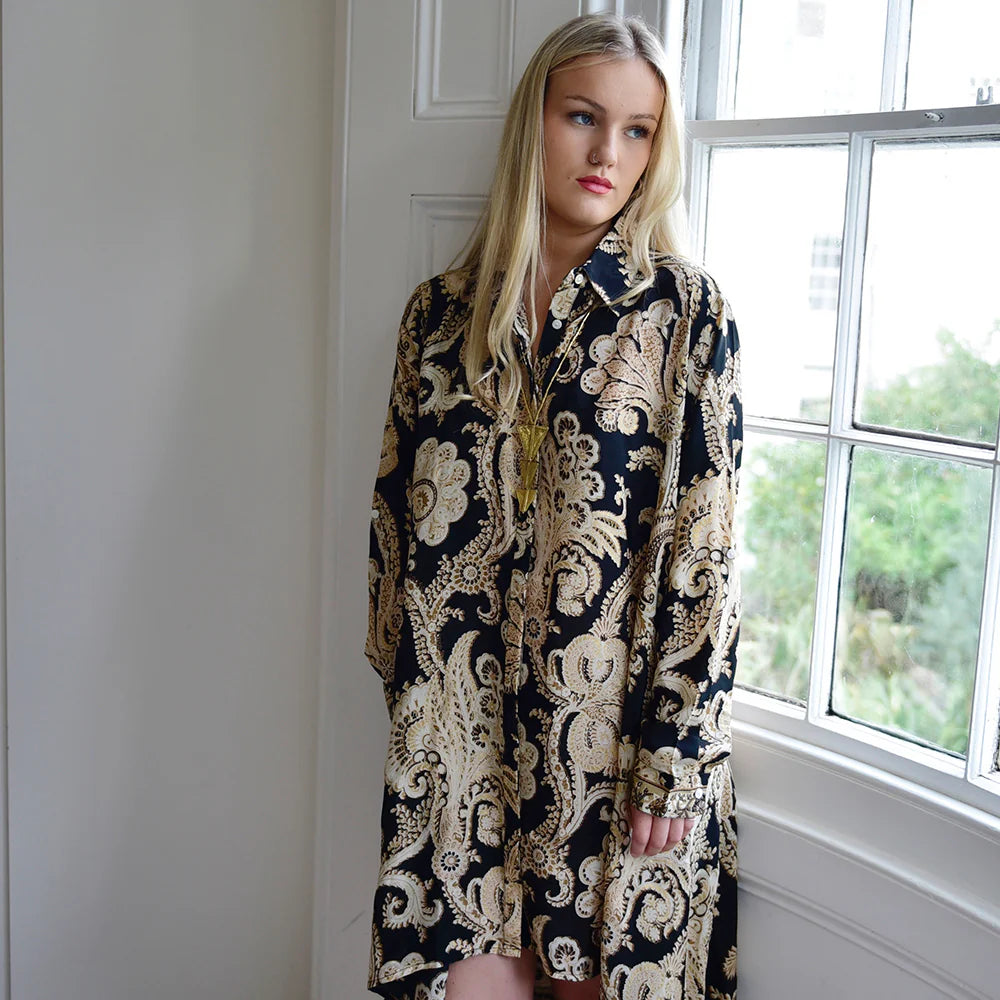 Woman wearing a black and gold dress standing in a room with a window.