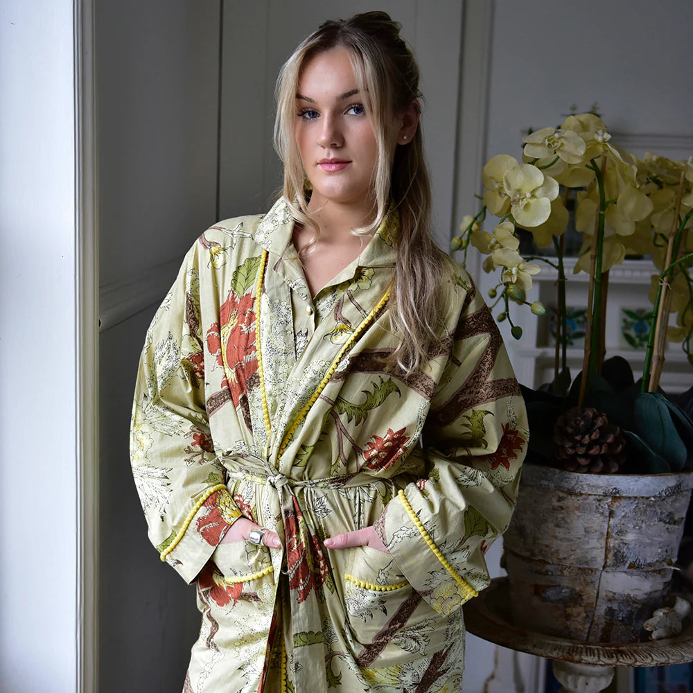 Woman wearing a Botanical Print Dressing Gown in a room with orchids.