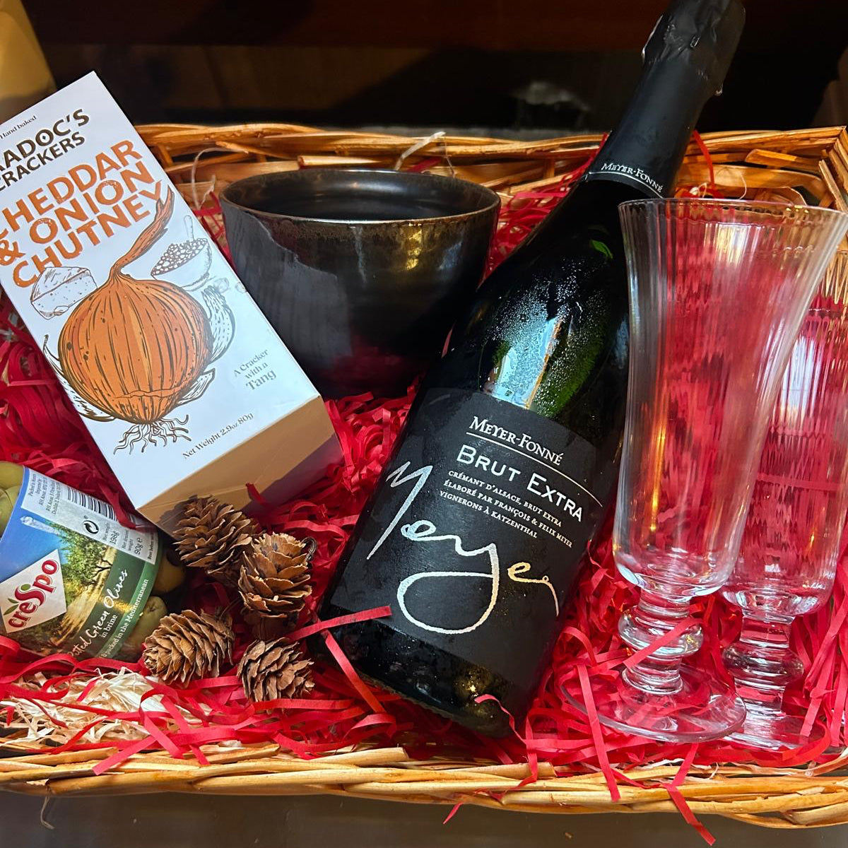 The Black Faced Sheep Festive Fizz Hamper, a bottle of Crémant, two champagne flutes and some crackers and olives and ceramic bowl.