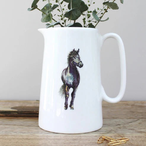 White ceramic pitcher with a horse design on a wooden surface with greenery in the background