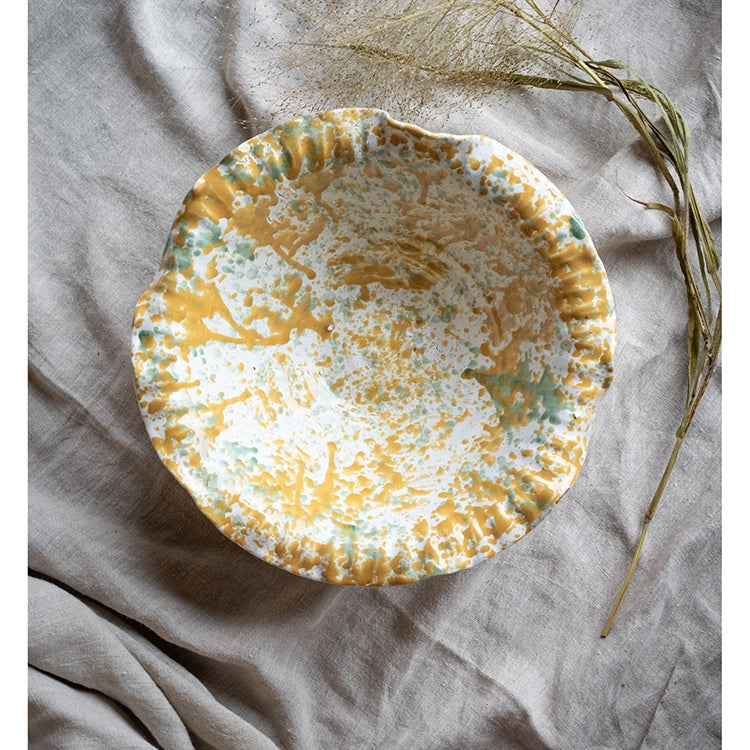 A yellow and green melange terracotta bowl with a leaf pattern on grey tablecloth
