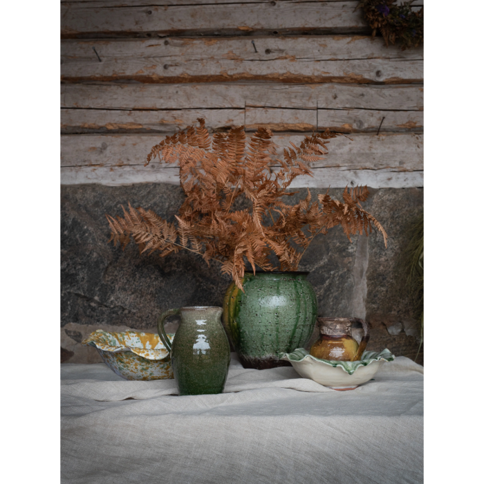Decorative setting with the Ivy ceramic bowl and other vases and a fern against a rustic wooden wall.
