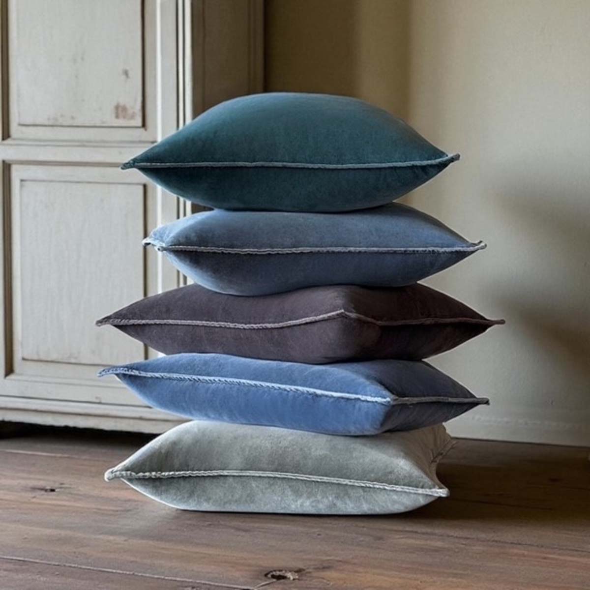 Stack of five blue, green, rust and grey cushions on a wooden floor.