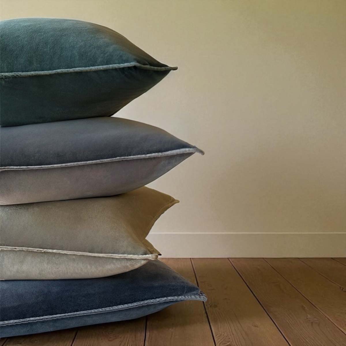 Detail of stack of velvet cushions in tones of green, grey and blue.