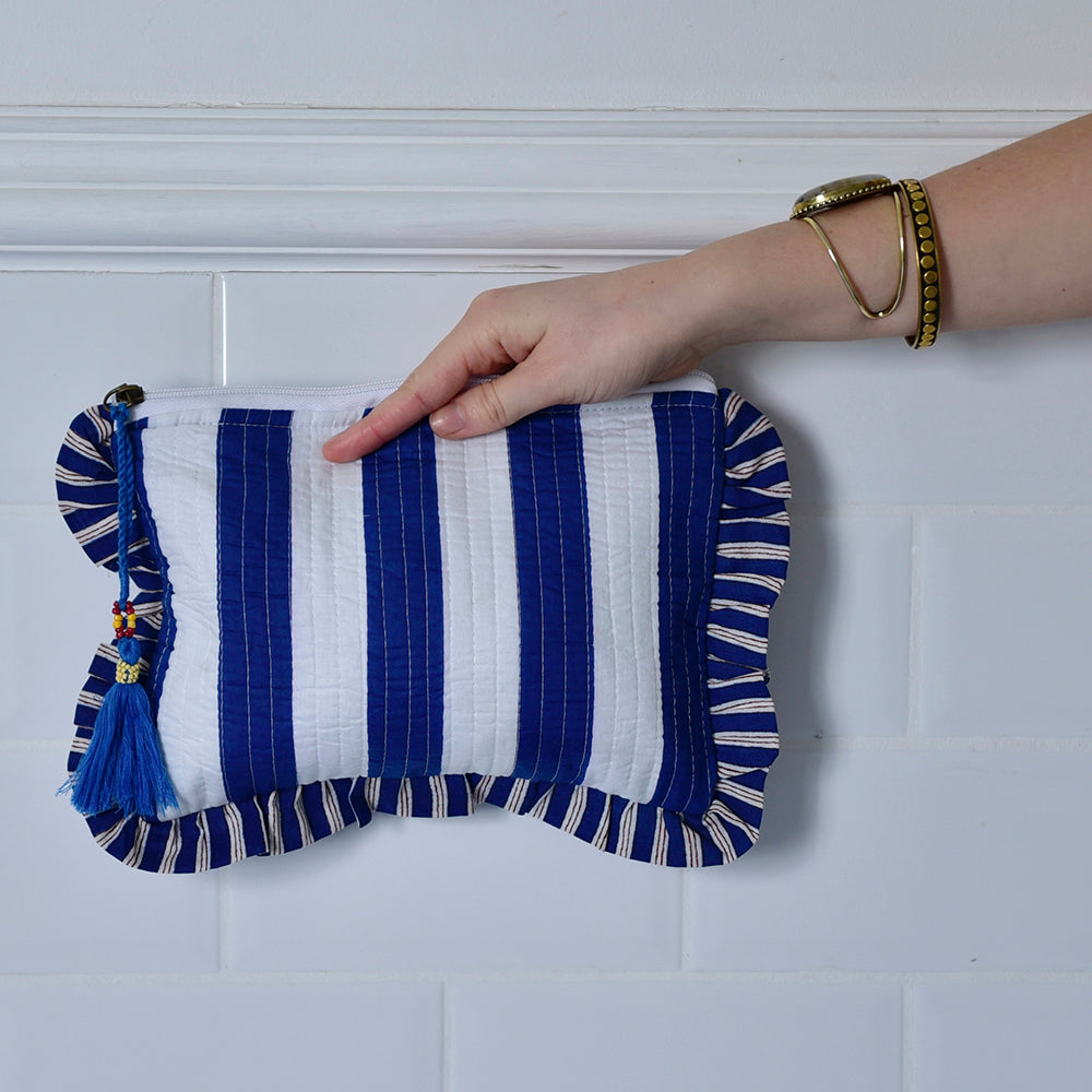 Blue and White Wide Stripe Seashell makeup bag back view of stripes held by hand against a white tiled background