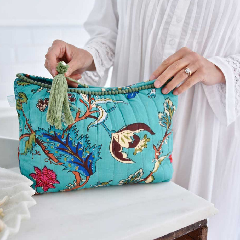 A person holding a teal wash bag with an exotic flower print and a fringed tassel.