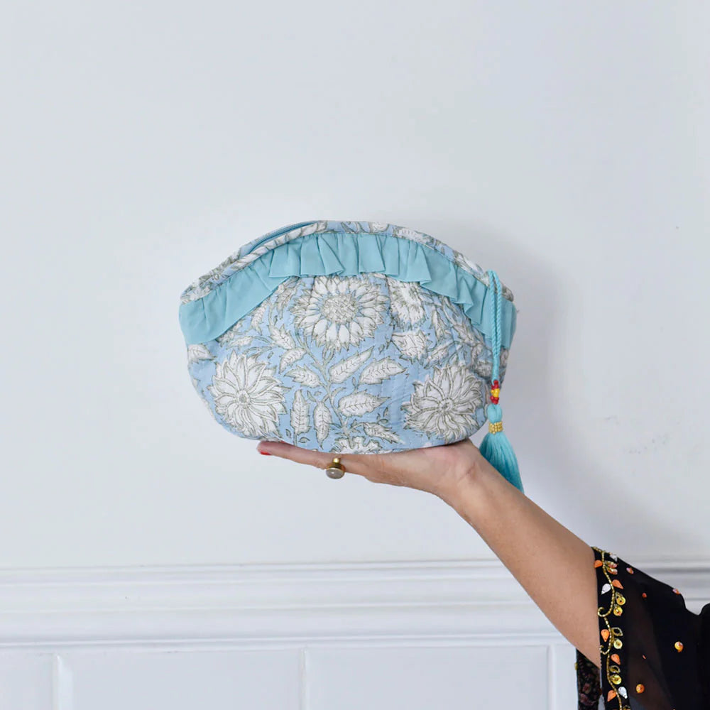 Hand holding a cornflower blue floral-patterned fabric wash bag against a white background