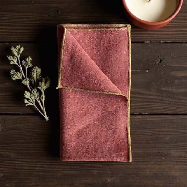Rust coloured napkin with gold piped edges.