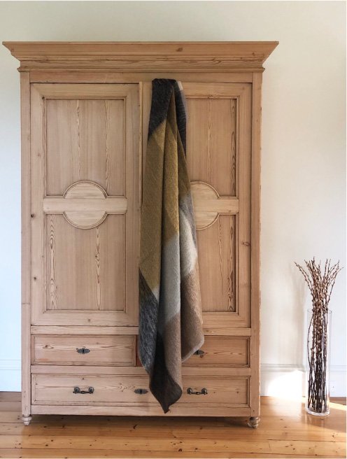 Luxurious mohair throw made in Scotland using traditional technique in honeycomb colours of ochre, grey and brown hanging from door of antique pine wardrobe..