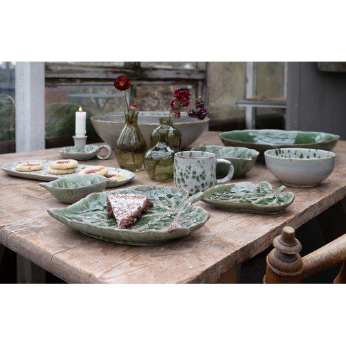 Aila porcelain green speckled bowls and cups on off-white background on a rustic table.
