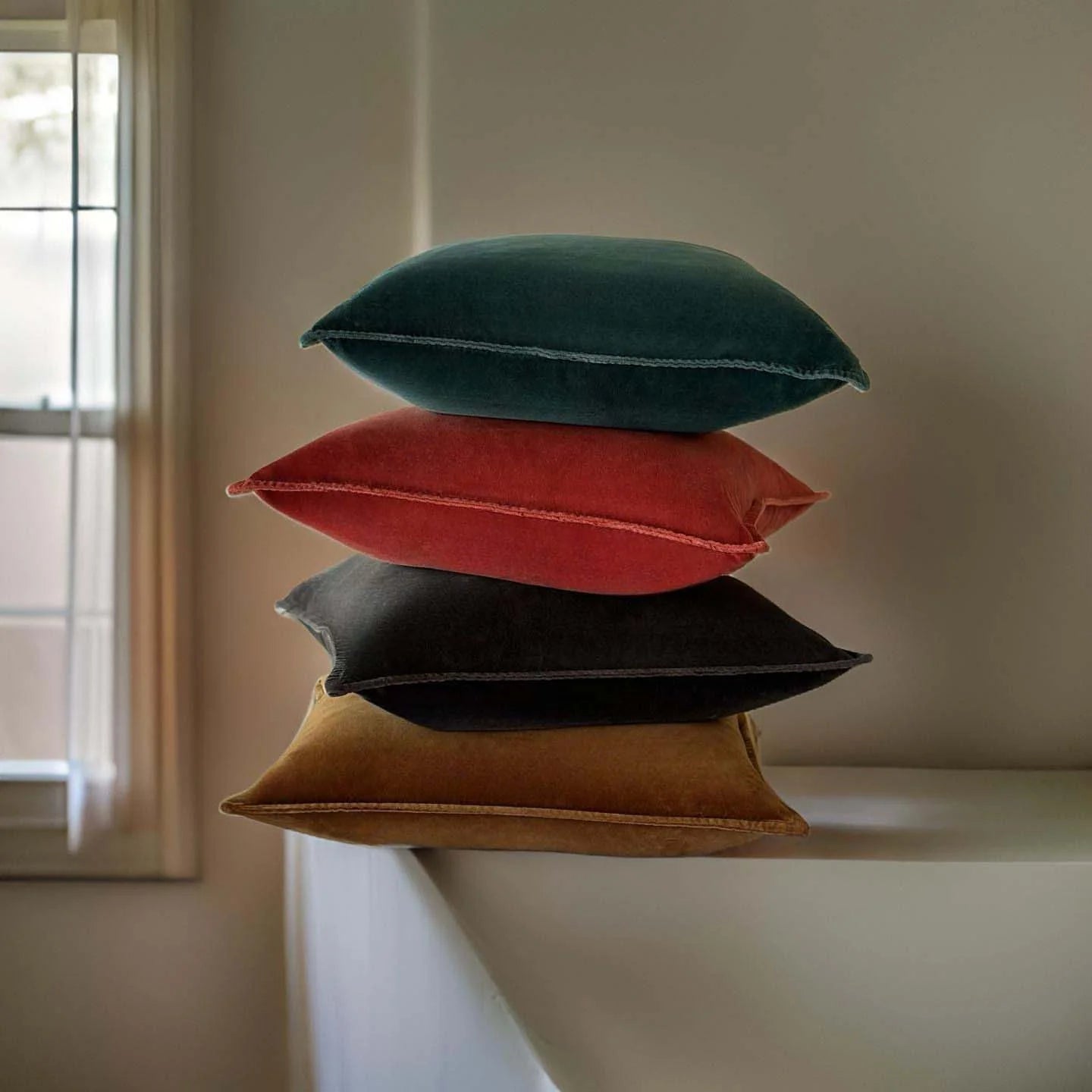 Selection of square velvet cushions in green, rust, black and brown.