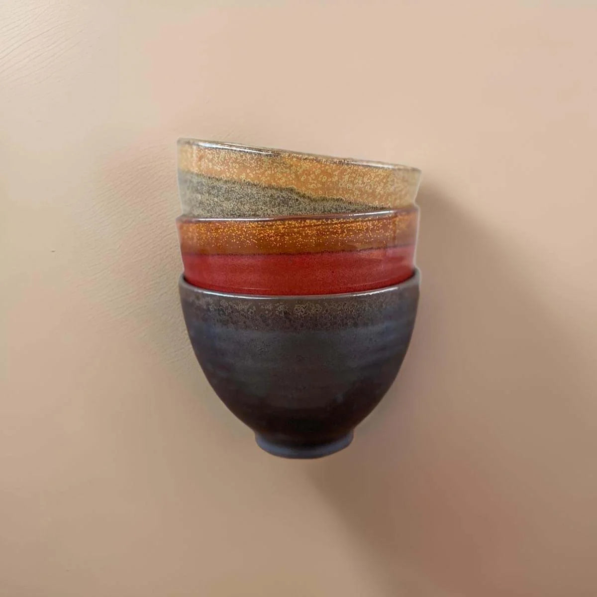 Stacked ceramic bowls with gold, rust and graphite glaze on a beige background