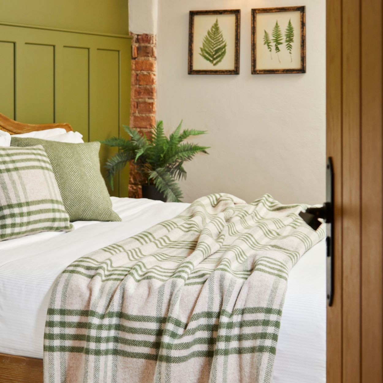 Detail of Olive Hex Wool Throw on bed with potted fern and pictures on the wall | Black Faced Sheep