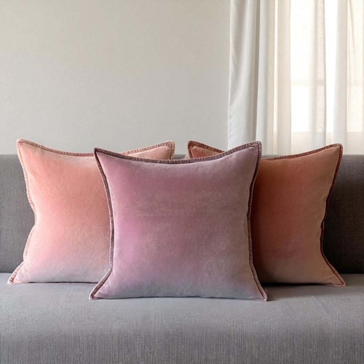 Three shades of pink velvet cushions on a gray sofa with a neutral background