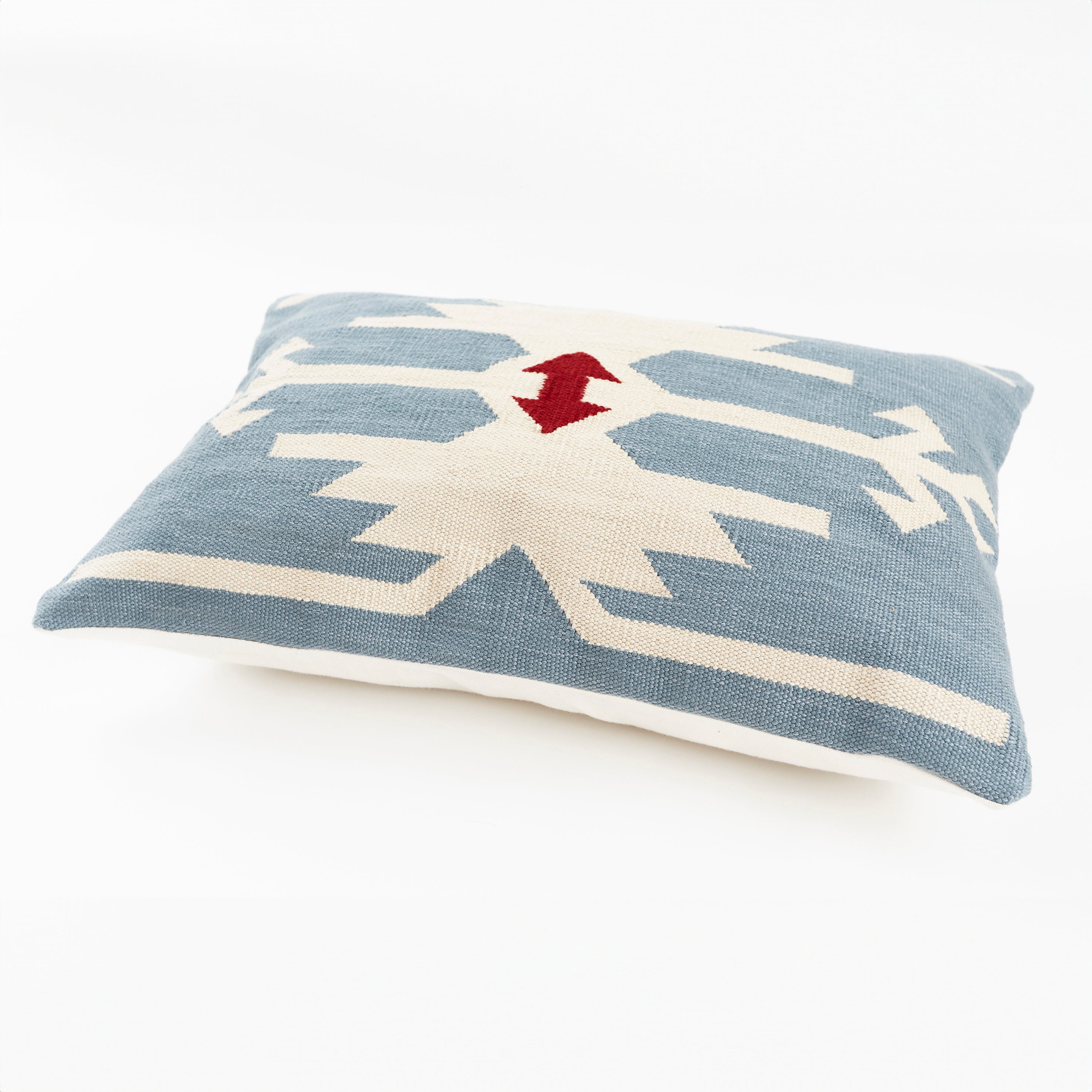 Detail of kilim inspired geometric patterned sofa cushion showing rectangular shape. Mid blue background with pattern in cream and red double arrow motif.