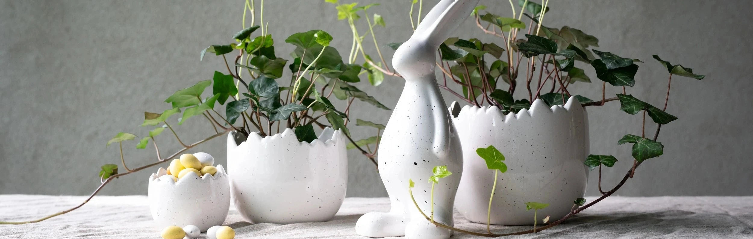 Decorative scene with ceramic rabbit and egg-shaped planters on a textured surface.