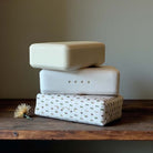 Stack of three rectangular soaps on a wooden surface with a neutral background.