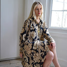 Woman wearing a black and gold dress sitting in a room with a window.