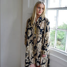 Woman wearing a black and gold dress standing in a room with a window.