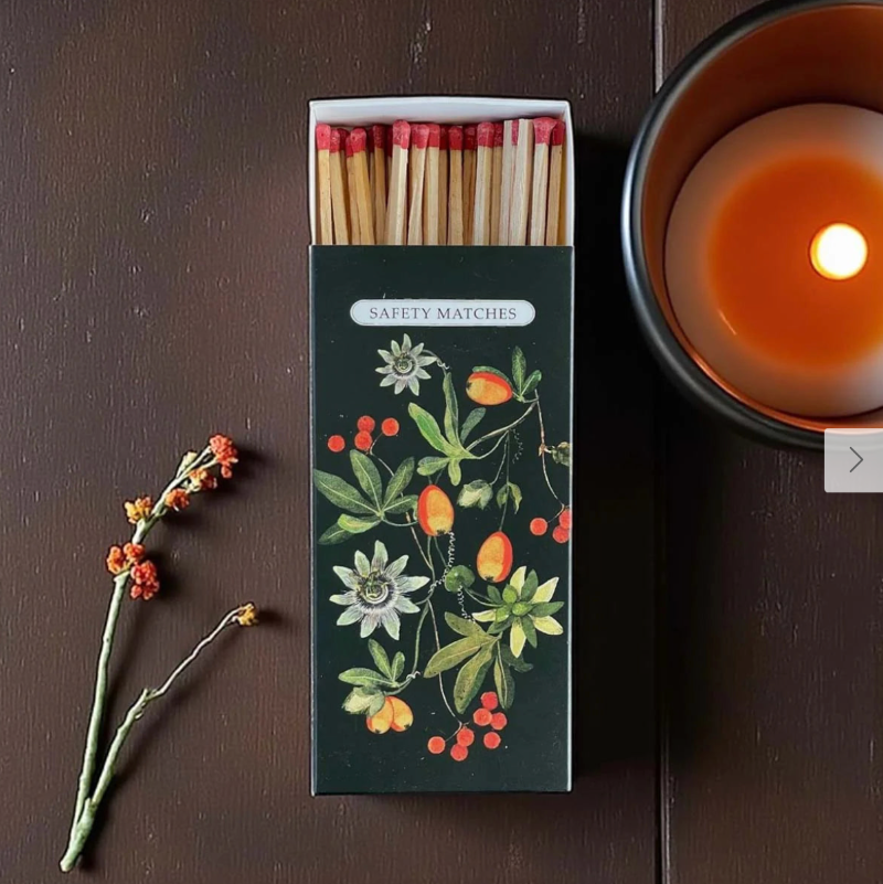 Matches with decorative packaging on a wooden surface next to a lit candle.