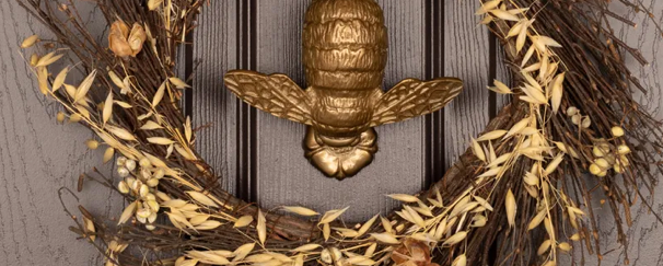 Decorative wreath with a gold bee and dried flowers on a wooden surface