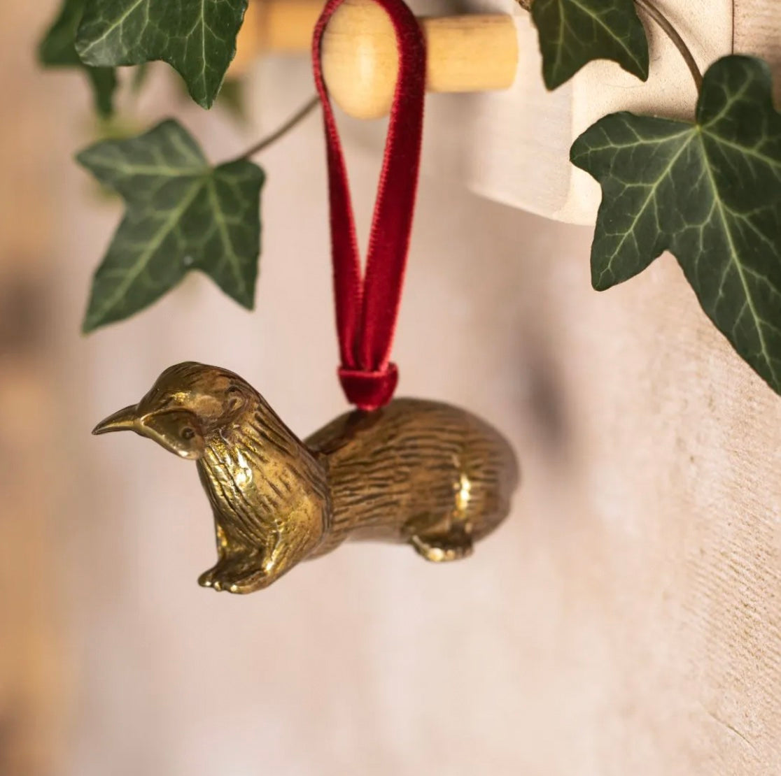 Brass otter-shaped Christmas ornament on red ribbon.