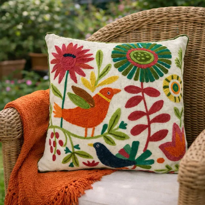 Decorative throw cushion with floral and bird patterns on a wicker chair outdoors.