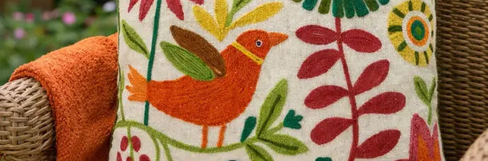 Decorative pillow with embroidered floral and bird patterns on a wicker chair outdoors.