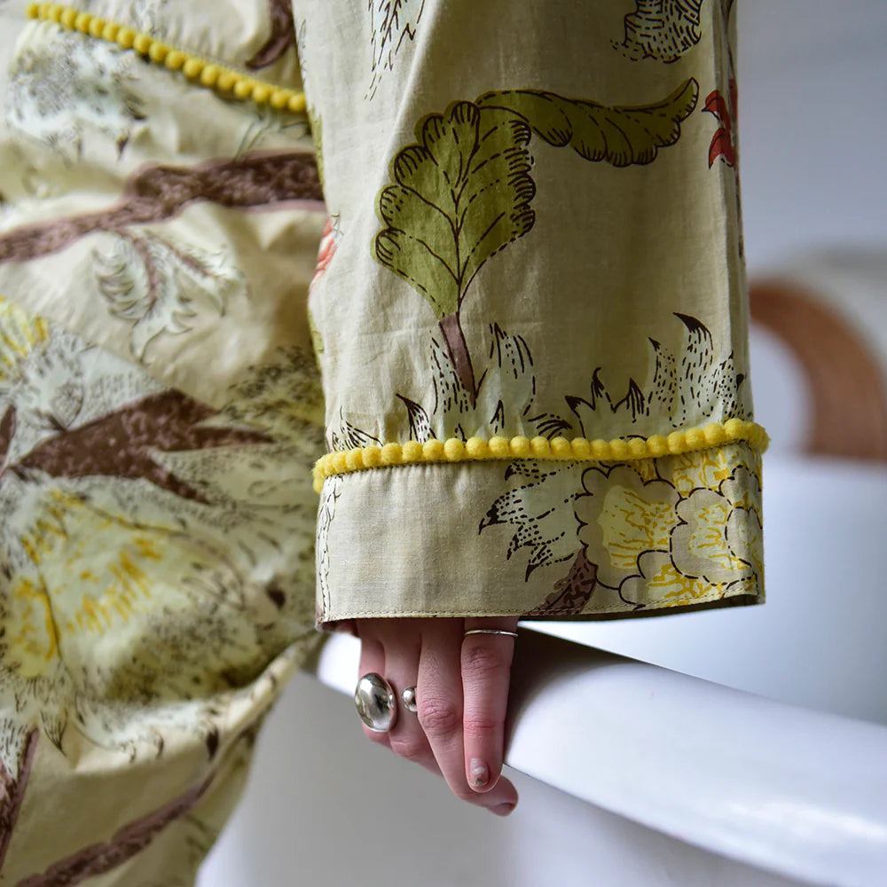 Close-up of a person wearing The Botanical Print Dressing Gown showing the yellow pom pom trim.