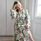 Woman wearing a floral patterned robe in a room with white walls and wooden floor.