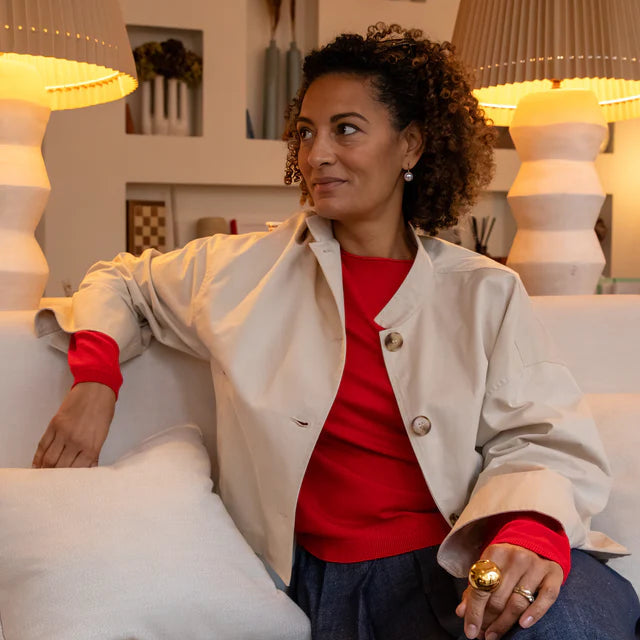 Woman sitting on a couch wearing a cotton jacket over a red shirt, with a neutral background.