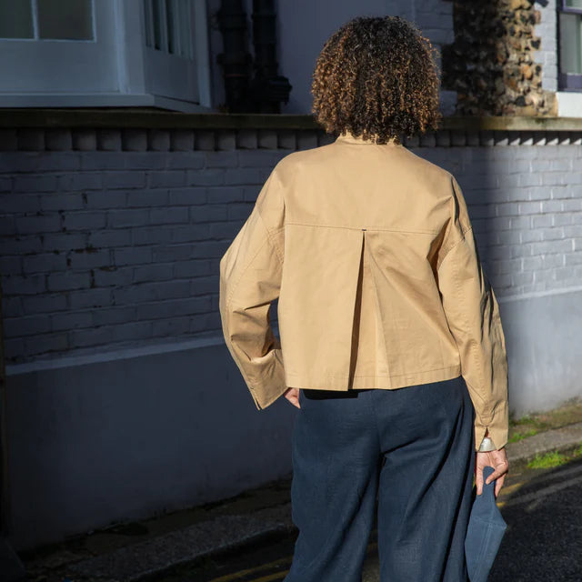 Person wearing a beige jacket and dark pants standing on a street.