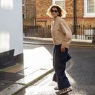 Woman walking on a street wearing sunglasses and a beige jacket.