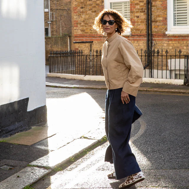Woman walking on a street wearing sunglasses and a beige jacket.