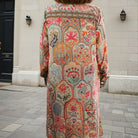 cream orange long, patterned dress standing on a street.