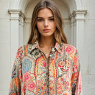 Woman wearing a colorful patterned shirt standing in front of a classical building.