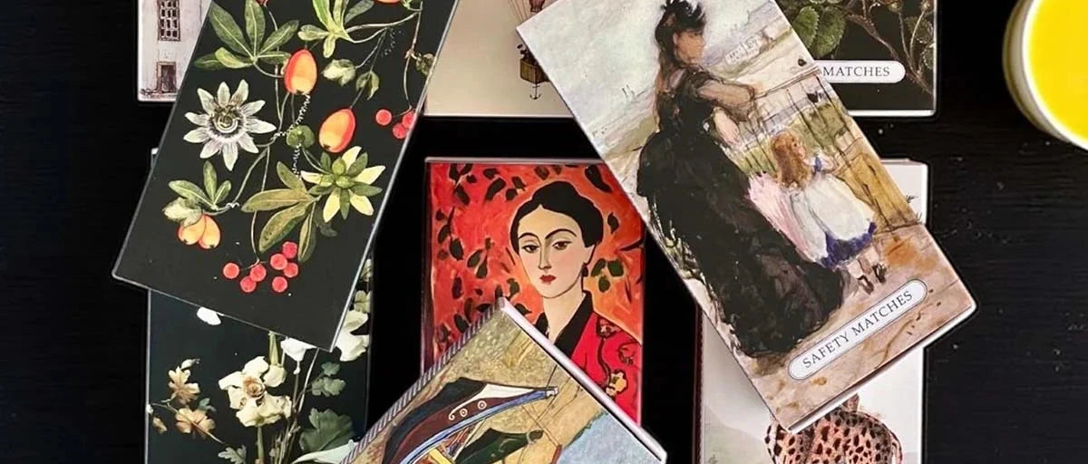 Collection of vintage-style matchboxes with artistic designs on a black surface.