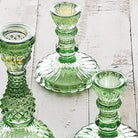 Three Tilda green glass candle holders on a white wooden surface