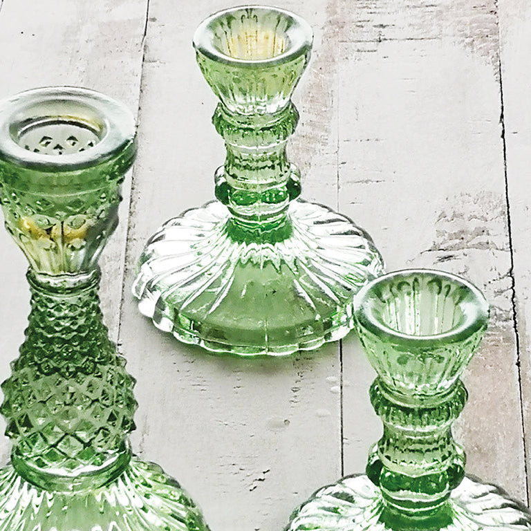 Three Tilda green glass candle holders on a white wooden surface