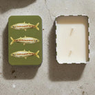 Candle in a tin with fish design on a textured surface