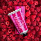 Hand cream tube labeled 'Jam Packed' on a bed of raspberries