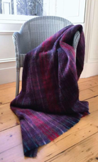 Traditionally made in Scotland our luxurious Mohair Throw in Sloeberry Colours (purple, pinks, reds) laid across a Lloyd loom chair.