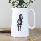 White ceramic pitcher with a horse design on a wooden surface with greenery in the background