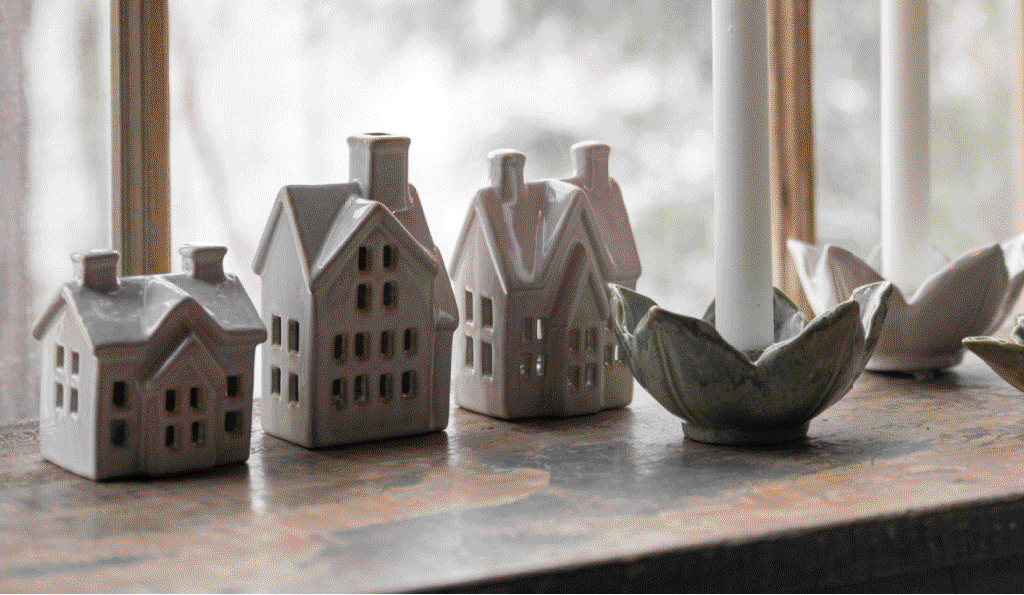 Decorative ceramic houses and candles on a table with a window background