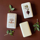 Three bars of soap with botanical designs on a brown background including beetroot and lime scented.