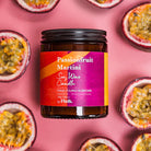 Passionfruit Martini candle jar with a pink label on a pink background with passionfruit halves.